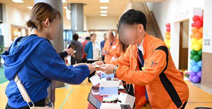 2025 秋季フーズフェアの受付でスタッフが来場者に印刷された入場パスを渡している写真