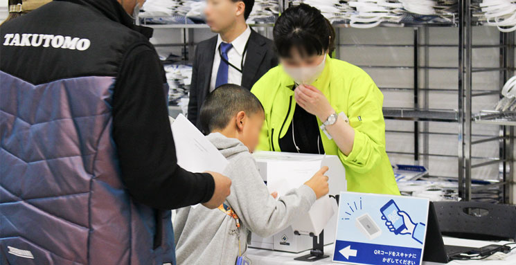 東京にぎわい市の会場入口で来場者が紙に印刷した2次元コードをスキャンして受付をしている風景