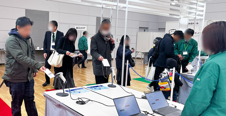 SANWA展示会の会場入口で来場者が事前に印刷した入場証をスキャナにかざして受付をしている風景