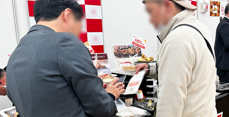 SANWA展示会で出展者が伝票を登録するためにスマホで来場者の入場証記載のQRコードを読み取っている様子