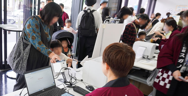 第11回住まいお宝発見フェアの会場入口でプリンターから入場証（かみのぱす）が印刷されている風景